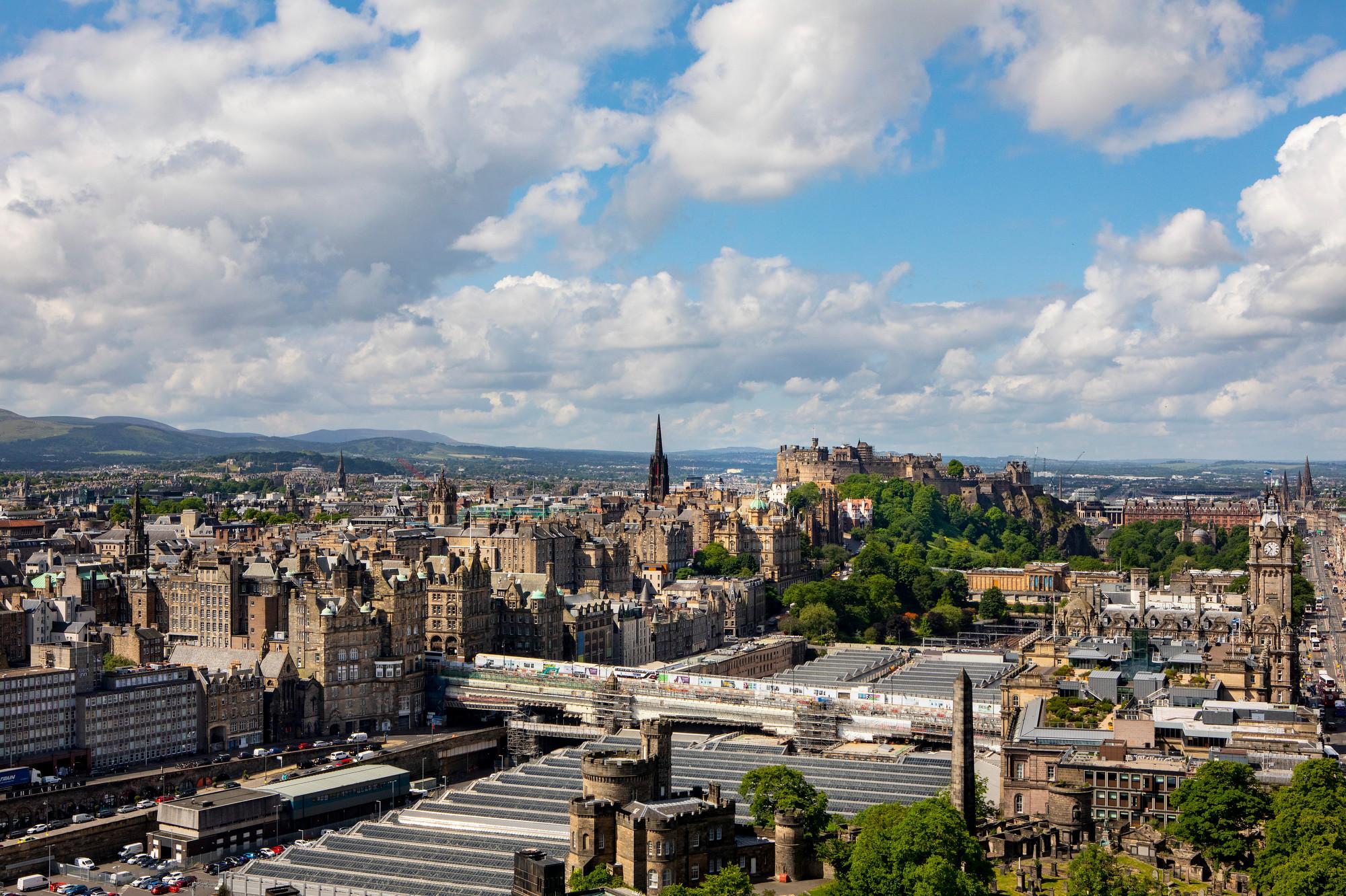 Skyline of Edinburgh from Calton Hill, it is a sunny day with some clouds. The Castle, Waverley Train Station and the Old Town are pictured.